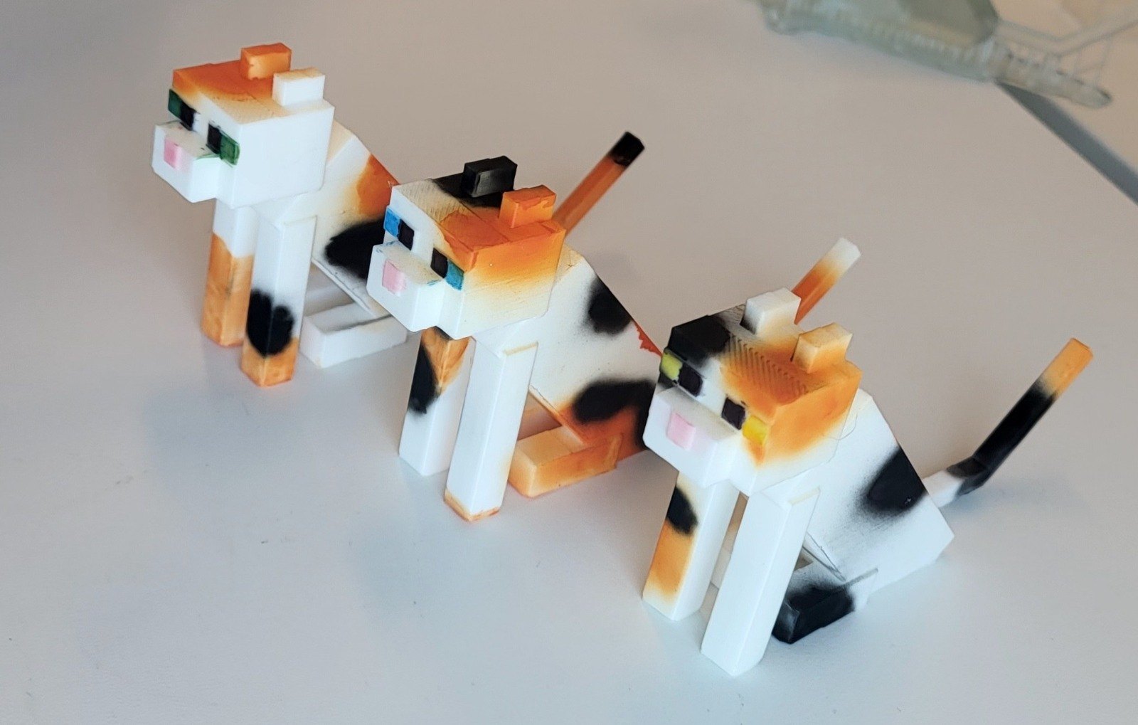 Three painted Minecraft cat models, printed in one piece and hand painted in white, orange and black.