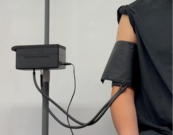 The non-invasive cuff fitted on an upper arm, tubing running to the pole-mounted monitoring enclosure.