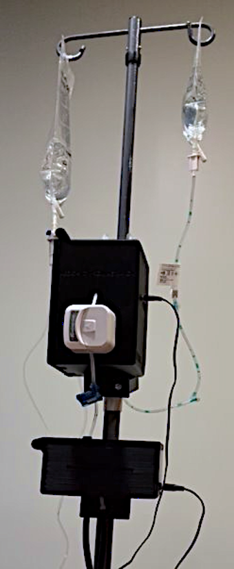 The full system mounted on an IV pole: monitoring enclosure, pump module, and infusion lines running to two bags.