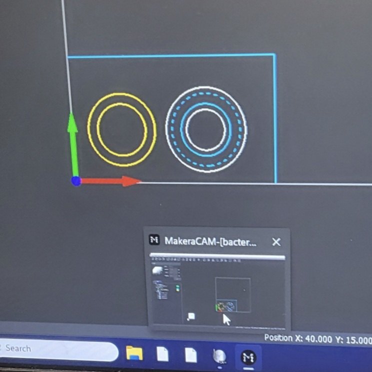 CAM software showing concentric toolpaths generated around two circular pockets, with the work origin and axes marked at the corner of the stock.