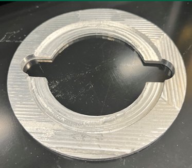 A machined aluminium ring off the mill, concentric tool marks across the face and two small slots cut into the bore.