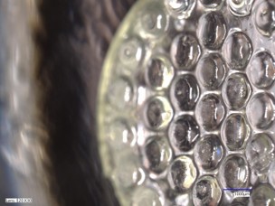 Micrograph of the moulded microlens array, the close-packed plano-convex lenses filling the frame with a scale bar at the lower edge.