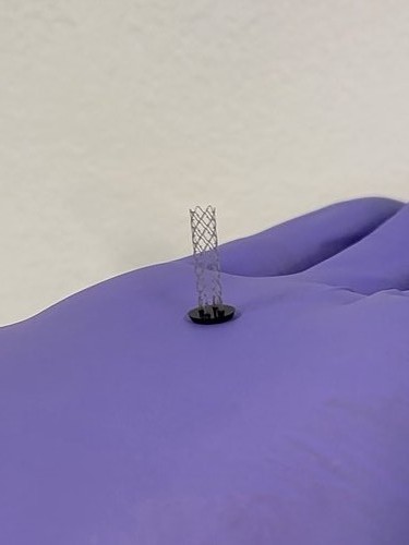 A finished MAP device held between two gloved fingertips, a few millimetres across.