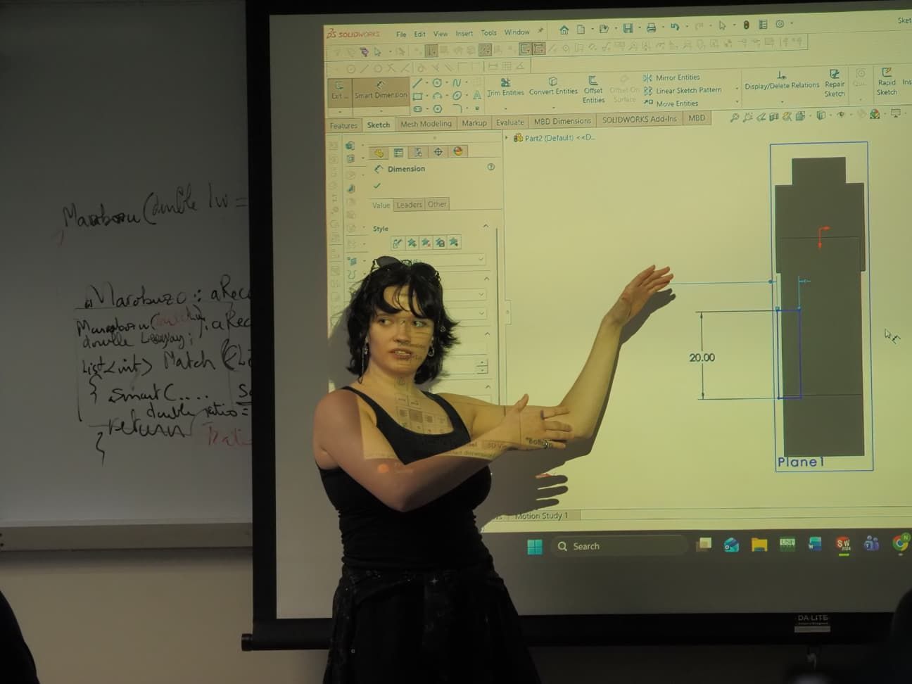 Teaching a parametric SOLIDWORKS sketch, dimensioning an extruded profile on the projected screen.