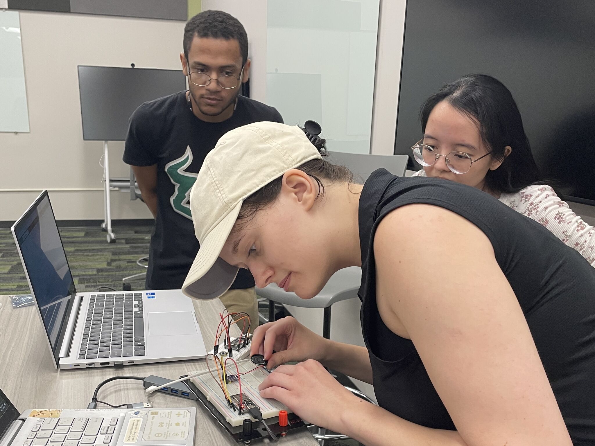 Wiring a speaker into an ESP32 breadboard build while two attendees look on.